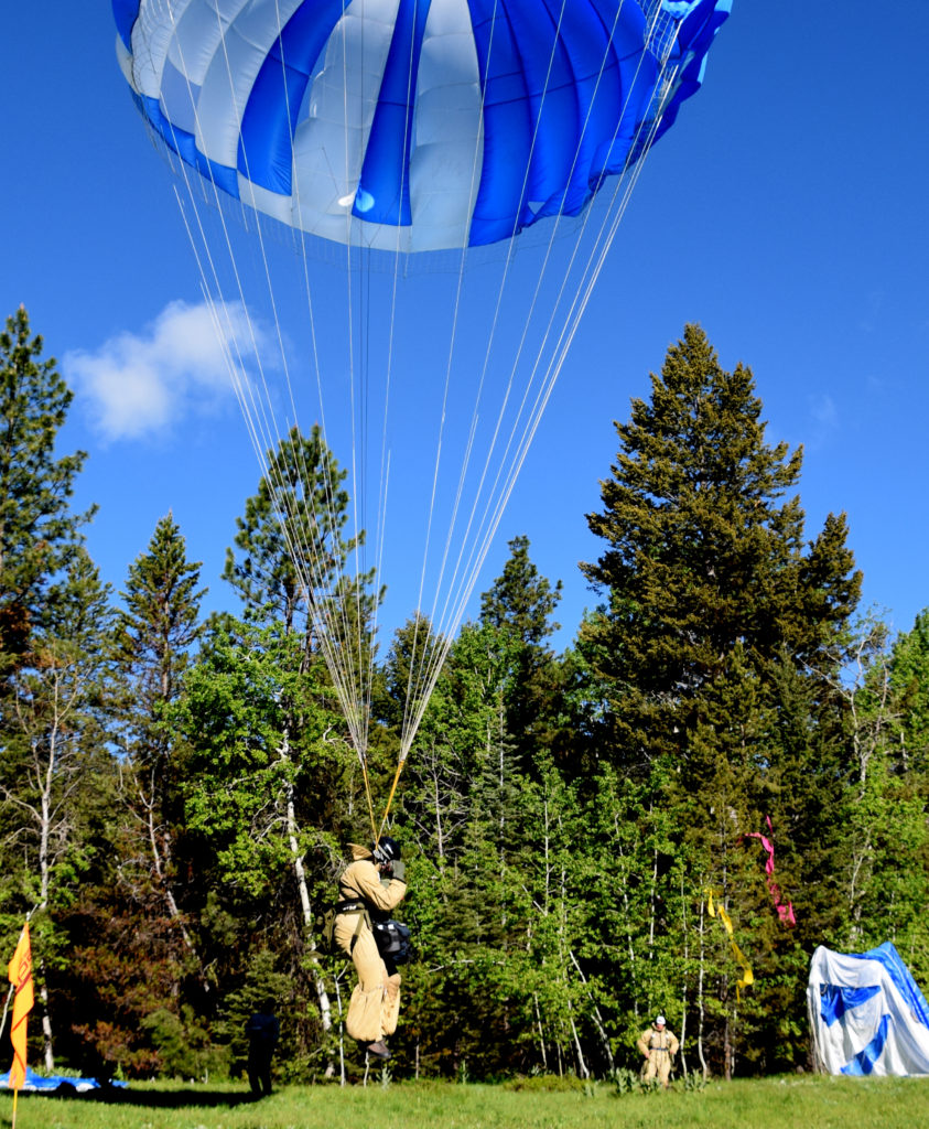 Almost down and ready for the ground roll. Note the yellow and pink crepe streamers in the trees in the background. Typically 2 sets of streamers are dropped prior to the jumps so that the pilot and spotter can determine wind speed and direction.