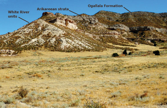 High Plains escarpment of Tertiary rocks on the eastern flank of the Laramie Mountains near Chugwater Creek. Eocene White River mudstone and siltstone, beds are capped by coarse sandstone beds. An overlying gravelly sandstone unit, probably of the upper Oligocene Arikaree Formation lies above the White River beds. The Miocene Ogallala Formation of stacked conglomerate sheets caps the entire section.